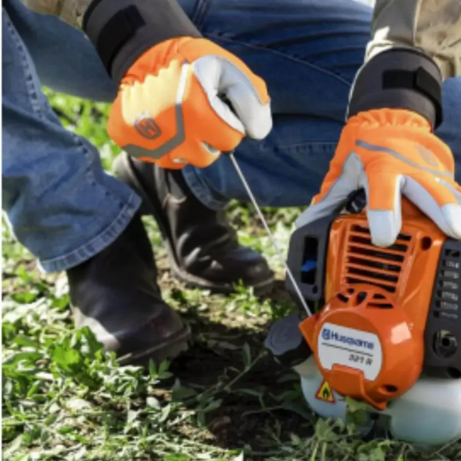 Detalhe do motor da Husqvarna 321R sendo ligado com a corda de partida, com o operador usando luvas de proteção
