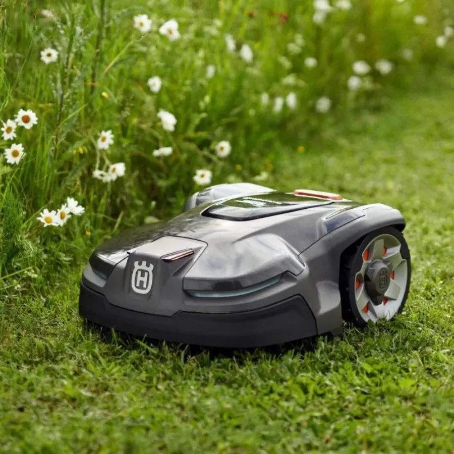 Robô cortador de grama Husqvarna Automower AM415X em uso real na grama, ao lado de flores